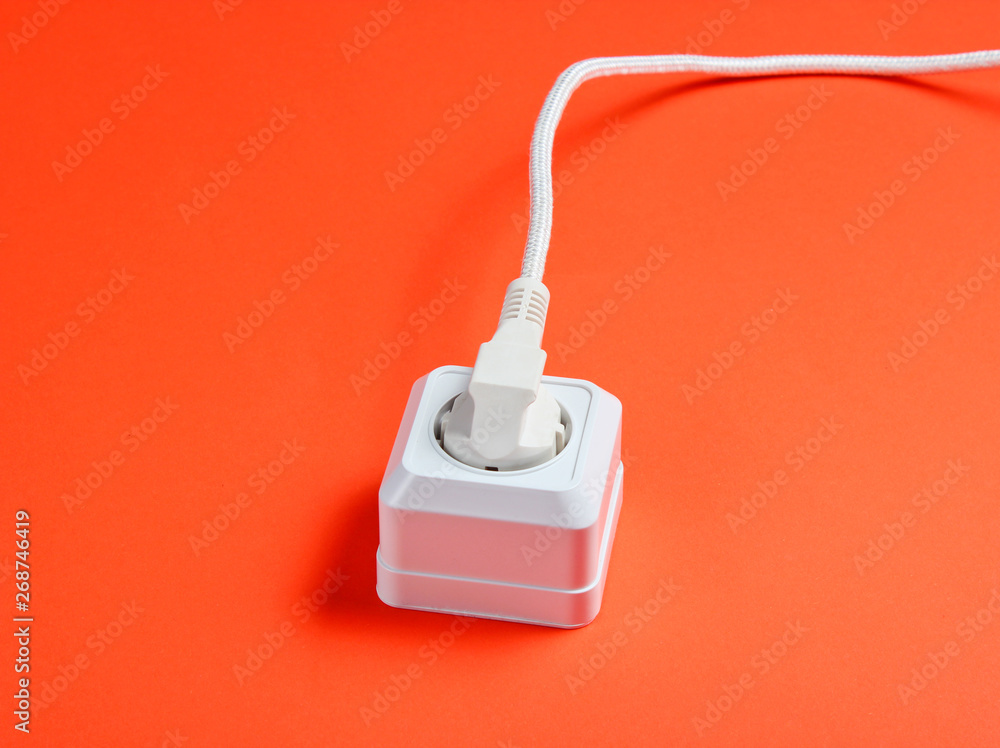 White cable plugged into power outlet on orange background White cable plugged into power outlet on orange background