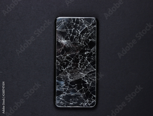 Smartphone with broken protective glass on black background photo