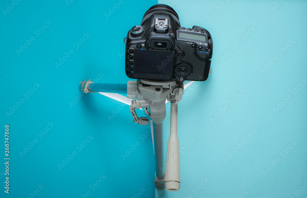 Modern digital camera with tripod on blue background. Top view Modern digital camera with tripod on blue background. Top view