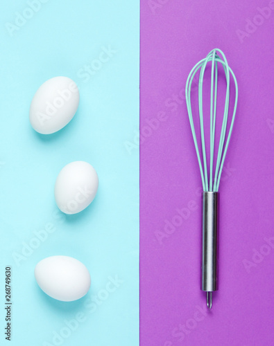 Kitchen whisk  chicken eggs on pastel colored background. Top view