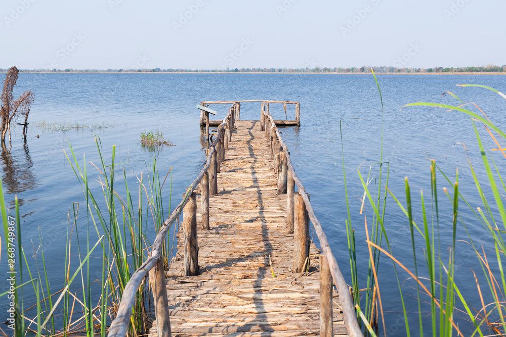 Naklejka premium Wooden bridge in forest in spring time with blue lake.