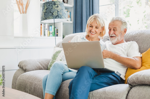 Couple senior using computer laptop on sofa at home for online shopping, surfing internet