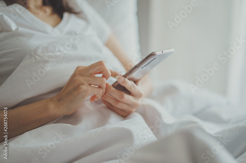 Asian Girl in bed room on the bed with the mobile phone.Closeup portrait of young sleepy exhausted woman lying in bed using smartphone 