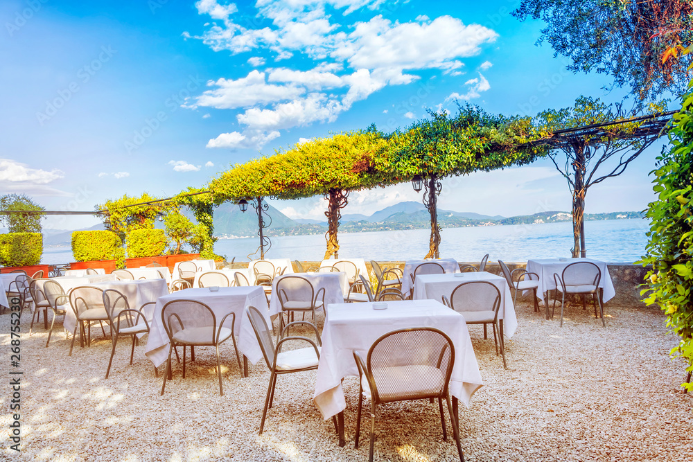 Outdoor restaurant with beautiful view on Lake Lago Maggiore in the background of the Alps Mountains at a sunny spring evening, Stresa, Italy