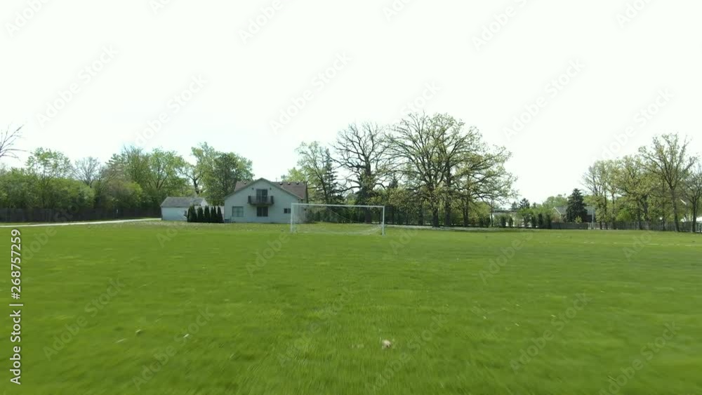 Forward moving shot across a soccer field through a ripped part of the net in the goal. No people, and a beautiful bright and sunny summer afternoon.