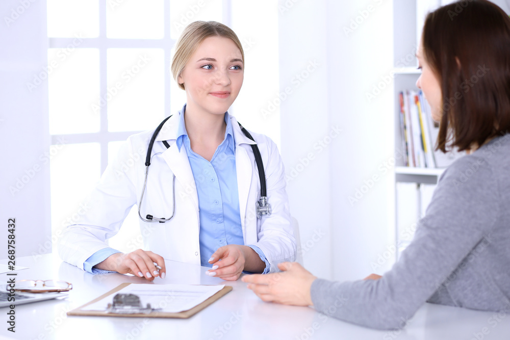 Young woman doctor and patient at medical examination at hospital office. Blue color blouse of therapist looks good. Medicine and healthcare concept Young woman doctor and patient at medical examination at hospital office. Blue color blouse of therapist looks good. Medicine and healthcare concept