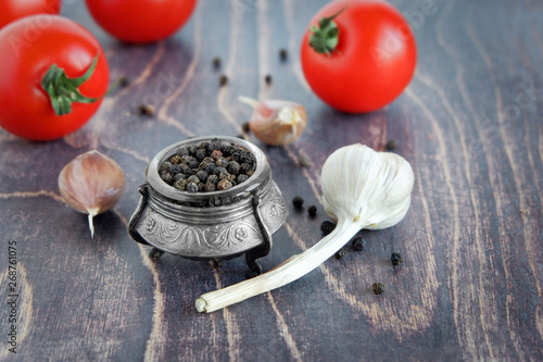 Black peppercorns, tomatoes and garlic cloves on a wooden table.