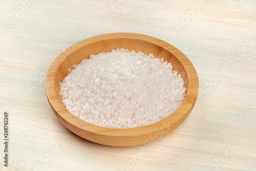 A closeup photo of a bowl of sea salt on a white wooden background