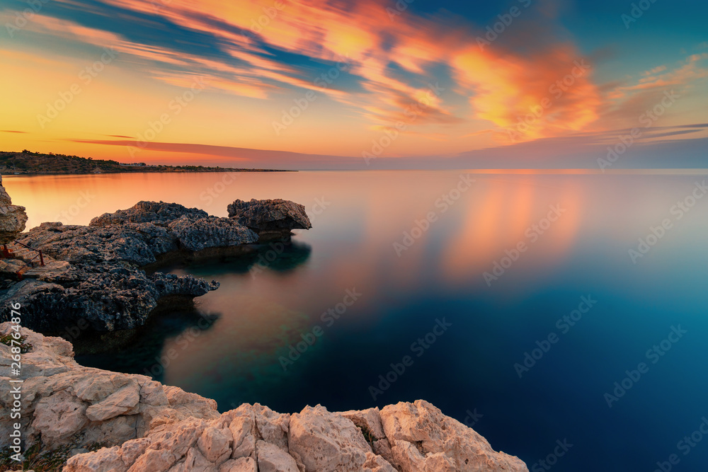 Amazing sunset image of Cape Greco cliffs and rocks on a sunset in Paralimni, Cyprus. Colorful red, pink and yellow skies with turquoise blue sea. 