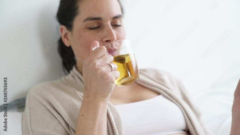 Pregnant woman laying on bed and drinking infusion Pregnant woman laying on bed and drinking infusion
