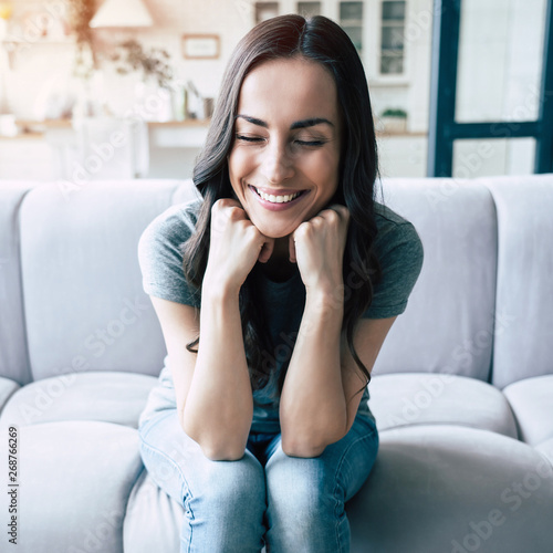 Portrait of smiling happy cute woman with closed eyes sitting on the couch at home