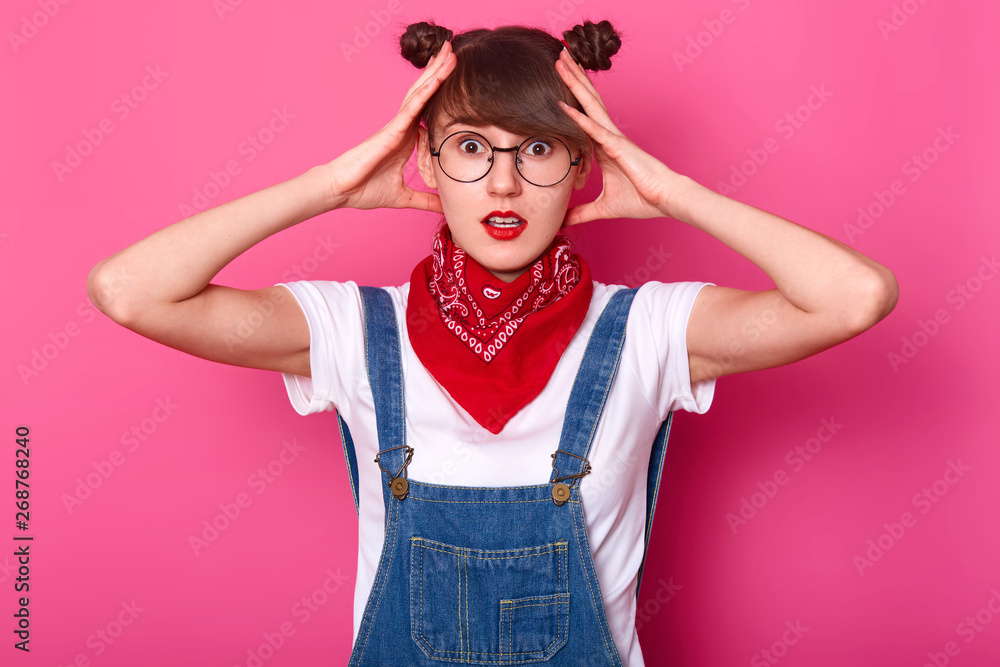 Shocked impressed young lady touching her head with both hands, opening her eyes and mouth widely, looking directlly at camera, being surprised, posing isolated over pink background in studio. Shocked impressed young lady touching her head with both hands, opening her eyes and mouth widely, looking directlly at camera, being surprised, posing isolated over pink background in studio.