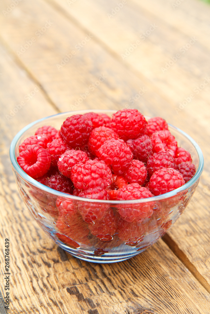 Ripe raspberries in the glass bowl on wooden boards. Ripe raspberries in the glass bowl on wooden boards.