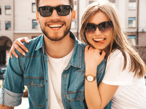 Portrait of smiling beautiful girl and her handsome boyfriend. Woman in casual summer jeans clothes. Happy cheerful family. Female having fun on the street background in sunglasses. Shows tongue