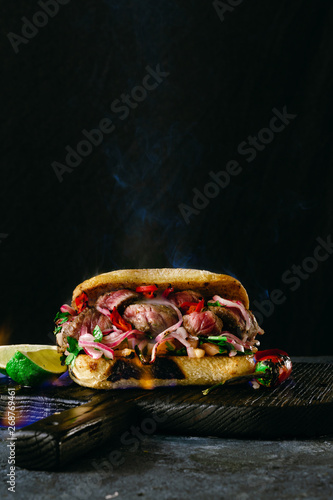 Grilled spicy steak sandwiches steak in fire flame on wooden cutting boards on dark background with copy space