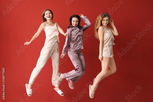 Jumping young women in pajamas near color wall