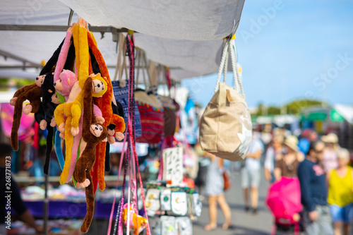 A flea market in Spain with stuffed animals, handbags, monkeys and gifts with many people in the blue sky and sunshine.