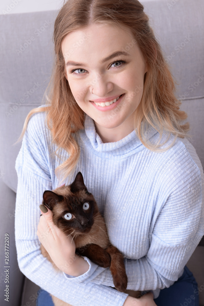 Young woman with cute Thai cat sitting in armchair Young woman with cute Thai cat sitting in armchair