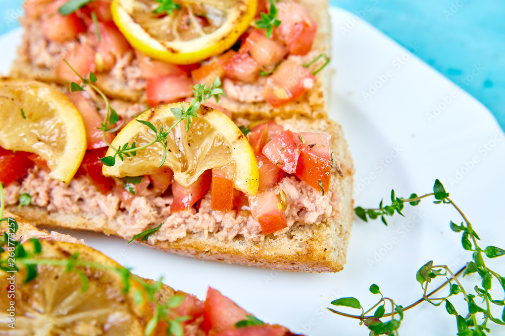 Appetizer bruschetta with tuna and tomatoes in white plate on blue background. Italian cuisine. Delicious Italian antipasti crostini. Copy space.