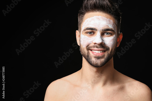 Handsome man with clay mask on his face against dark background