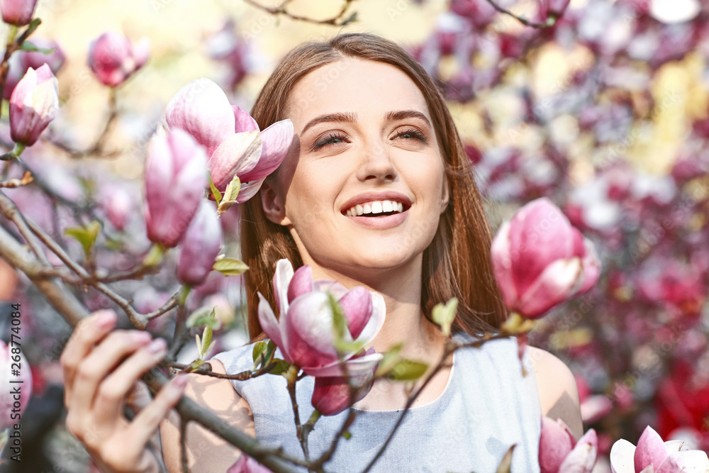 Fototapeta premium Portrait of beautiful young woman near blooming magnolia tree outdoors