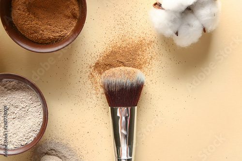 Cosmetic clays in bowls with brush on color background