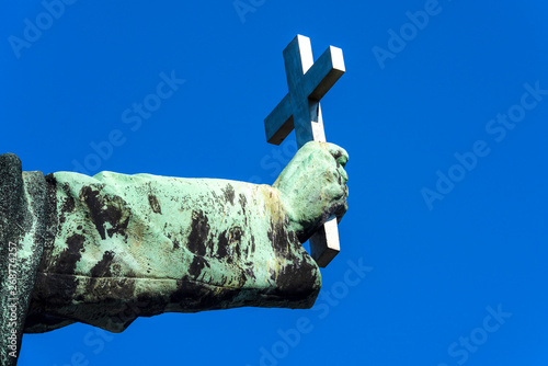 Holy Christian cross in copper rust covered hand isolated on blue sky background - concept Christianity Catholicism religion Christ god church forgiveness exorcism belief faith strength prayer worship photo