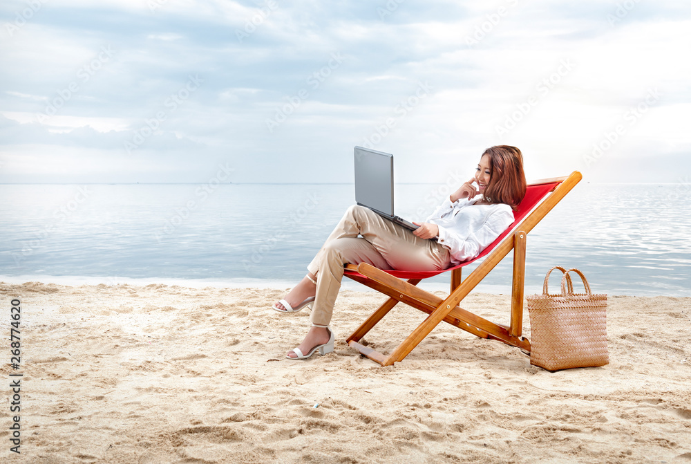 Asian business woman working with laptop sitting in the beach chair on beach
