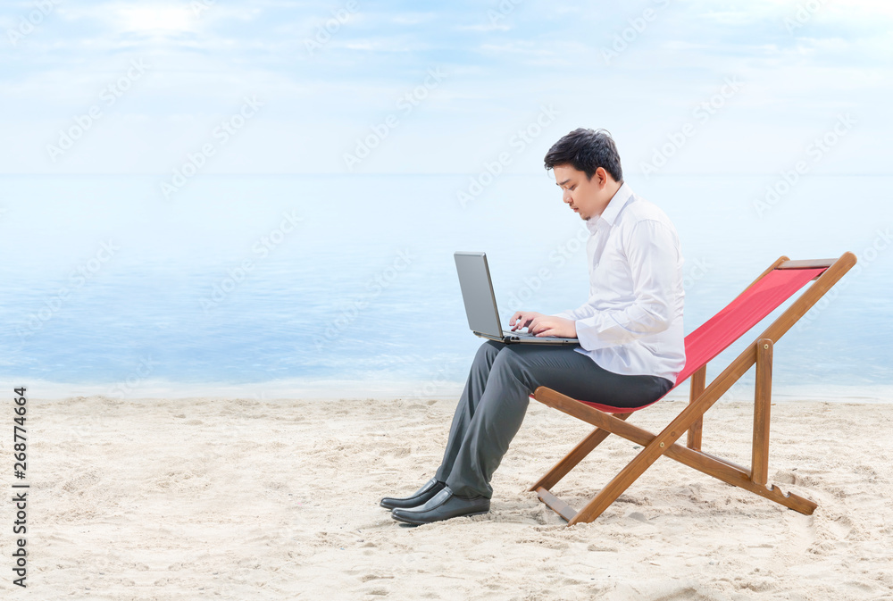 Asian businessman working with laptop sitting in the beach chair on beach