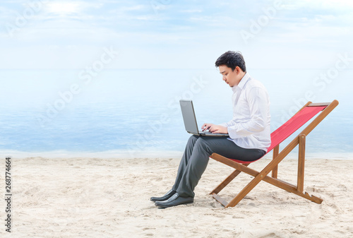 Asian businessman working with laptop sitting in the beach chair on beach