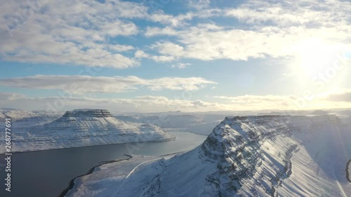 Aerial, drone shot towards a rocky mountain ridge, overlooking snowy fjords and the arctic sea, on a sunny evening, at isafjardardjup, in Westfjords, Iceland photo