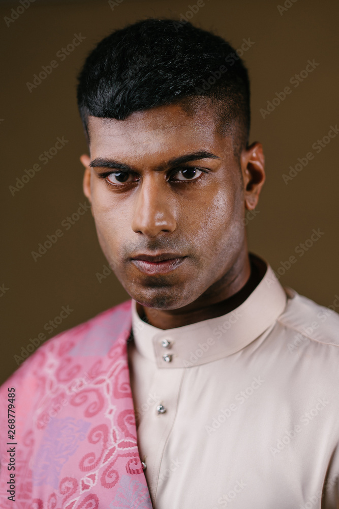 Portrait of a young and handsome Malaysian Indian Muslim man in a cream colored traditional baju melayu outfit with a striking pink sash. He is dressed festively to go visiting for Raya. Portrait of a young and handsome Malaysian Indian Muslim man in a cream colored traditional baju melayu outfit with a striking pink sash. He is dressed festively to go visiting for Raya.