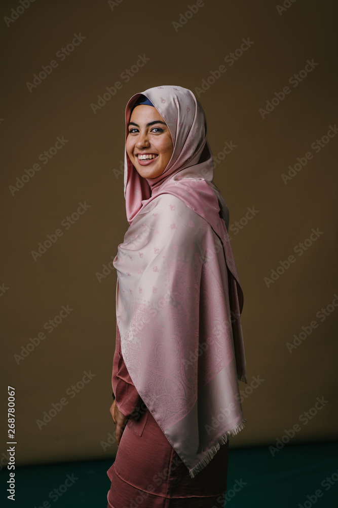 Studio portrait of a startlingly beautiful, vital and attractive young Middle Eastern Muslim woman in a pink, stylish, elegant and festive traditional baju kurung dress and hijab head scarf. Studio portrait of a startlingly beautiful, vital and attractive young Middle Eastern Muslim woman in a pink, stylish, elegant and festive traditional baju kurung dress and hijab head scarf.
