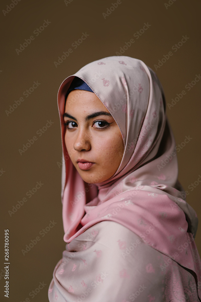 Studio portrait of a beautiful young woman in a pink shirt and a hijab head scarf. Studio portrait of a beautiful young woman in a pink shirt and a hijab head scarf.