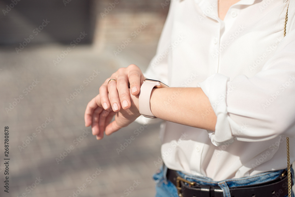 Woman wearing white shirt wearing blue jeans and a gentle nude manicure looks at the watch close-up