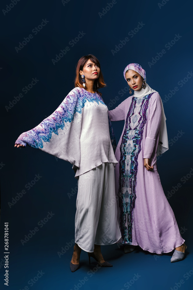 Two beautiful, elegant and attractive Malay Asian Muslim women in festive and traditional festive clothing for Raya / Eid / Ramadan. They are smiling and dancing. One is wearing a hijab headscarf. 