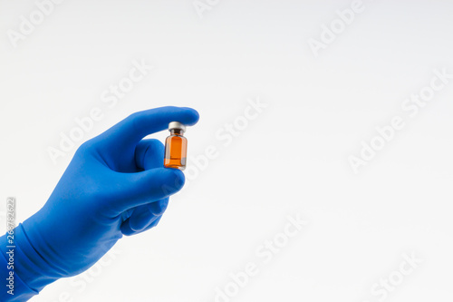 Hand in a blue glove holding medical vial isolated on white