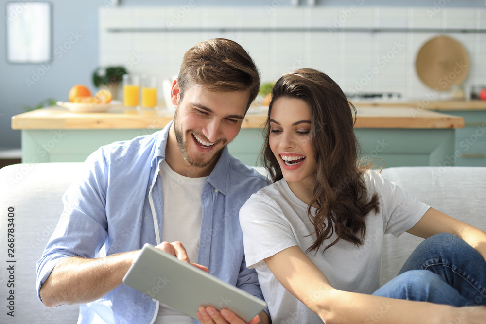 Young couple watching media content online in a tablet sitting on a sofa in the living room. Young couple watching media content online in a tablet sitting on a sofa in the living room.