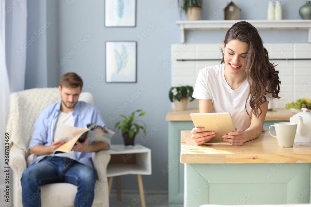 Smiling beautiful woman using laptop with blurred man in background at home. Smiling beautiful woman using laptop with blurred man in background at home.