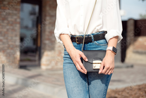 Young woman in jeans and a white shirt standing on the street holding a lady's bag in which lies her smart phone and wallet.