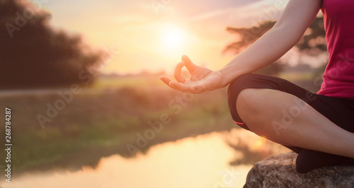 Woman yoga practicing and meditating by the lake in summer background