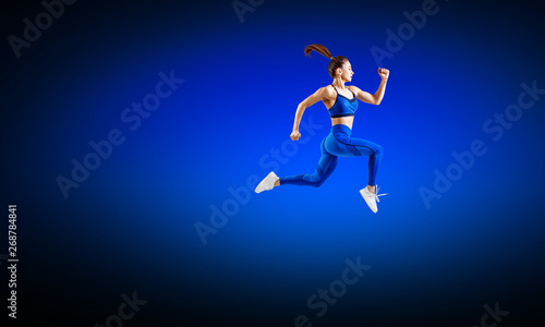 Young woman runner in blue sportswear jump in the air. © Dmitrii Kotin