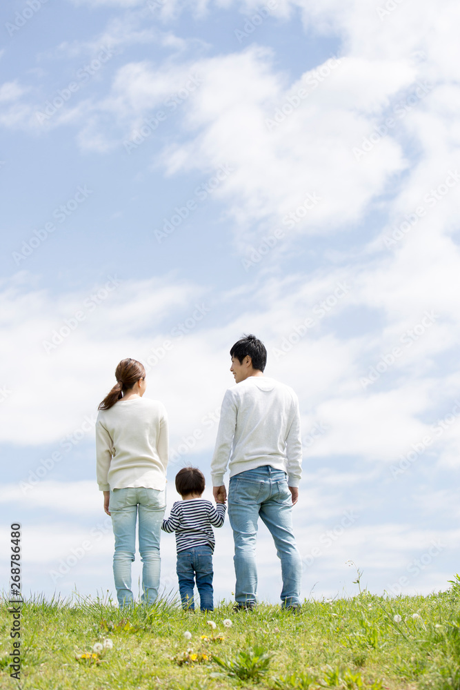 若い家族の全身後ろ姿、青空背景
