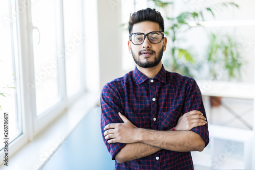 Portrait of a good looking smiling Indian man crossed arms standing at modern building office