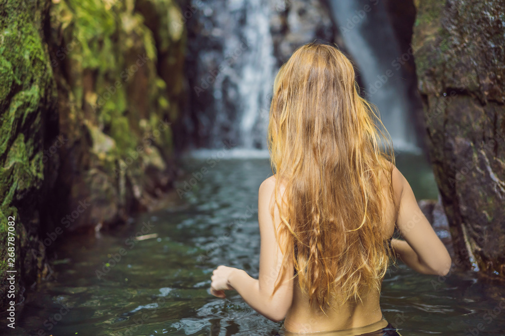 Fototapeta premium Young beautiful woman standing in the water at the waterfall