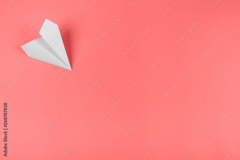 White paper airplane on the corner of the coral background - obrazy, fototapety, plakaty 