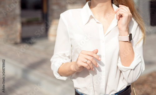 Portrait of a successful happy business woman in a white shirt and sunglasses. Smart watch on a hand stands at the entrance to the business center.