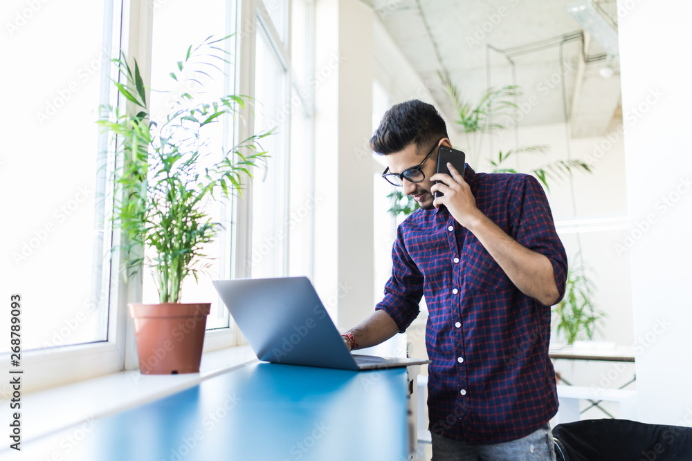 Indian businessman working on laptop and talking on the phone in modern office Indian businessman working on laptop and talking on the phone in modern office