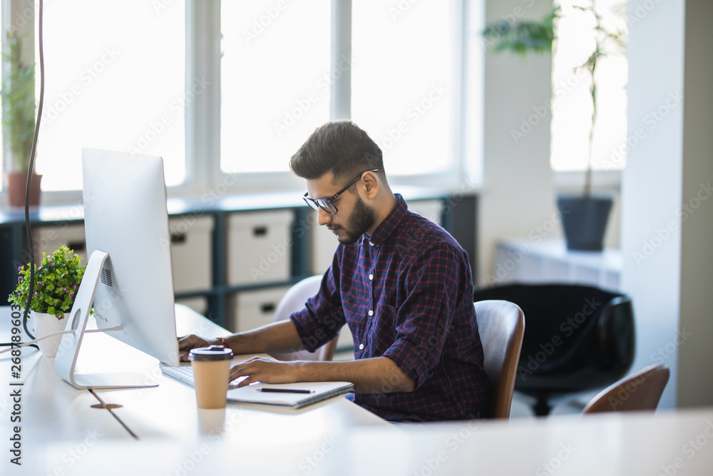Handsome young indian business man with working place in creative office Handsome young indian business man with working place in creative office