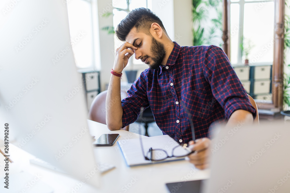 Fotografie Tired Indian male frustrated with work sitting in front of a laptop in office